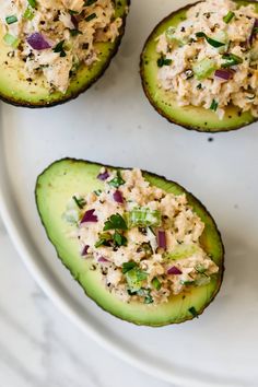 four stuffed avocados with tuna salad in them sitting on a white platter