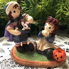 two figurines sitting on top of a table next to plants and pumpkins