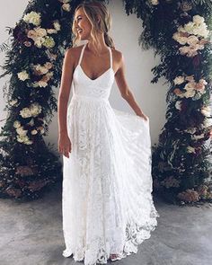 a woman wearing a white dress standing in front of a floral arch with flowers on it