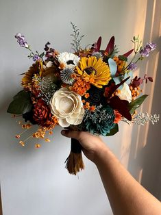 a hand holding a bouquet of flowers in front of a white wall with sunlight coming through the window