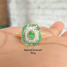 a close up of a person's hand holding a ring with an emerald and diamond center