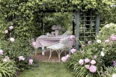 a table and chairs are in the middle of some bushes with pink flowers on it