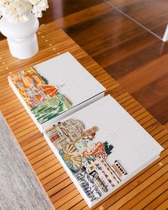 two notebooks sitting on top of a wooden table next to a vase with flowers