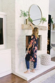 a woman standing in front of a fireplace with a mirror on the wall above it