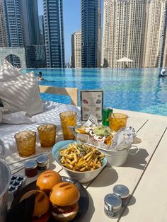 a table with food and drinks on it next to a pool in the middle of a city