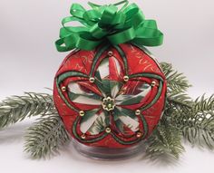 an ornament with a green bow on top of it sitting next to some pine branches