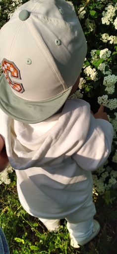 a small child wearing a hat and white pants in front of flowers on the ground