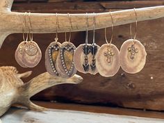 five pairs of earrings hang from a branch with a deer's antler in the background