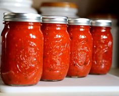 four jars filled with red sauce sitting on top of a counter