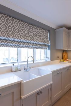 a kitchen with white cabinets and gray roman shades on the window sill above the sink