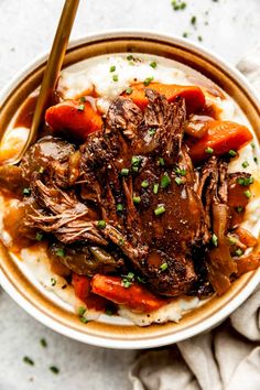 a bowl filled with meat, carrots and mashed potatoes on top of a table