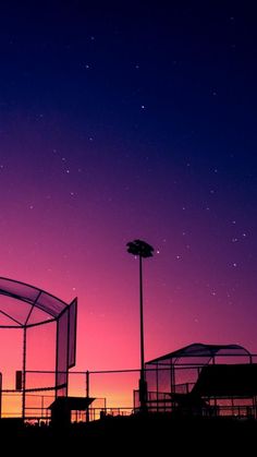 the sky is purple and pink with some stars in the night sky above it, as seen from behind a fence