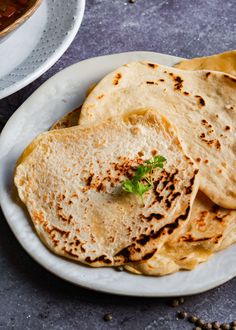 some pita bread on a white plate next to a bowl of beans and sauce