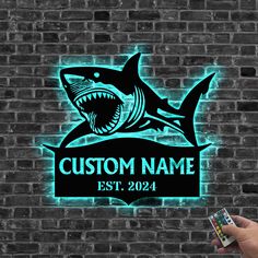 a hand holding a remote control in front of a brick wall with a neon sign that says custom name