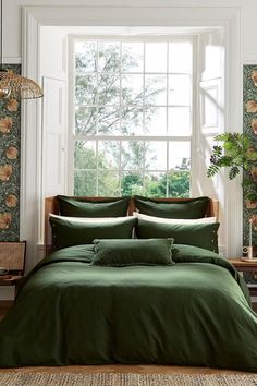 a bed with green sheets and pillows in front of a large window that has flowers on it