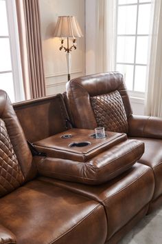 a brown leather reclining couch with a cup holder on the armrests in front of two windows