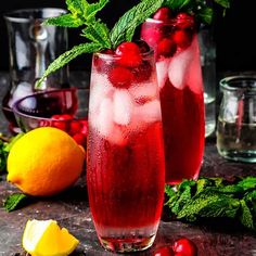 two glasses filled with red liquid next to lemons and mint