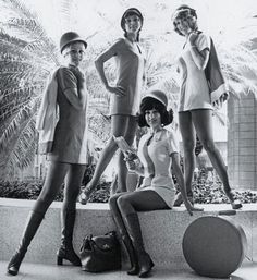 four women in short dresses and high heels posing for a black and white photo with palm trees in the background