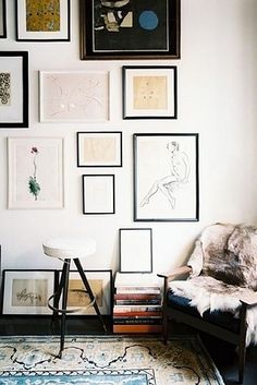 a living room filled with lots of framed pictures on the wall above a chair and table