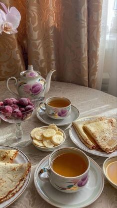 a table topped with plates of food and cups of tea next to a vase filled with flowers