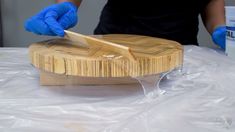 a person wearing blue gloves and rubber gloves is cutting wood with a sharp knife on a table