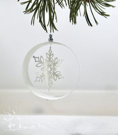 a glass ornament with a snowflake design hanging from a pine tree