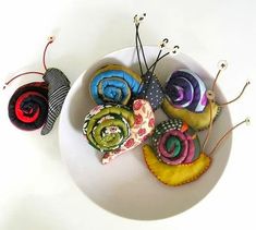 three snails are sitting in a bowl on a white surface next to two small pins