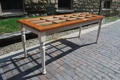 a wooden table sitting on top of a brick road next to a building with windows