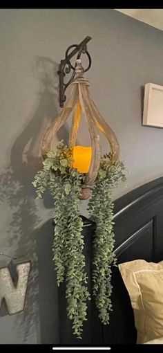 a lamp hanging from the side of a bed next to a wall with plants on it