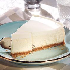 a slice of cheesecake on a blue plate with a fork and glass vase in the background