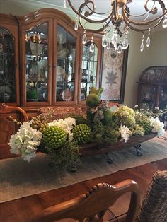 a wooden table topped with lots of flowers next to a china cabinet and chandelier