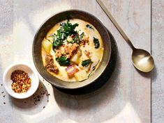 a bowl filled with pasta and spinach on top of a table next to a spoon