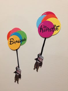 two colorful balloons with name tags attached to the handles on each balloon are hanging upside down