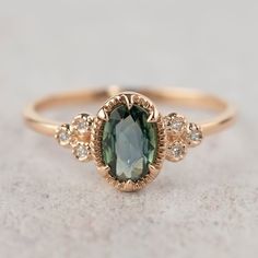 a ring with an oval green stone surrounded by small white diamonds on a gray surface