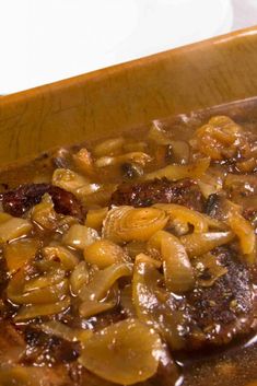 some meat and onions are in a brown sauce on a wooden tray with a spoon