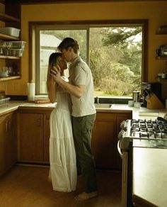 a man and woman standing next to each other in a kitchen near a stove top oven