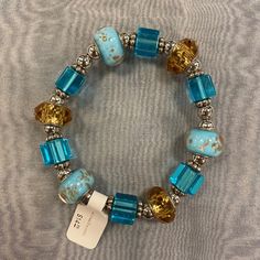 a blue and gold beaded bracelet on a gray cloth with a tag hanging from it