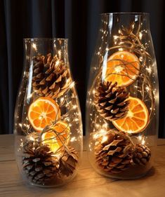 two glass vases with orange slices and pine cones on them, sitting on a table