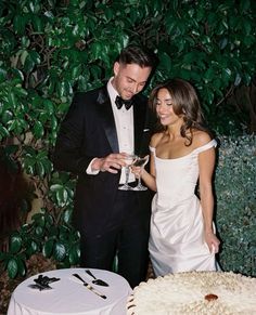 a man and woman standing next to each other in front of a cake