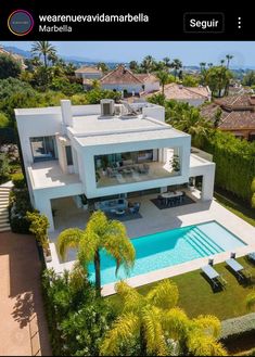 an aerial view of a house with a pool in the foreground and palm trees surrounding it