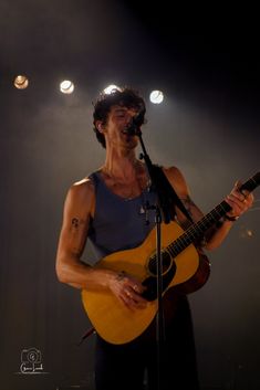 a man holding a guitar while standing in front of a microphone