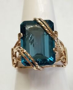 "London Blue at it's best  This is a \"PREMIUM COLOR\" 19.0 carat genuine London Blue Topaz wide band ring!  This stunning gem is a step-cut rectangle shape securely set in a rope overlay design.  The wire is \"jewelers preferred\" 14K Yellow Gold GF 20-gauge square wire.  The shank is \"SILK FIT\" for every day comfort.  This ring is designed and durable for everyday wear.   A Bold handsome ring for a man, but also a stunning and unique addition to a woman's jewelry wardrobe at a fraction of th Rectangle Topaz Ring, Luxury Modern Topaz Ring For Gift, Luxury Topaz Ring With Rectangular Gemstone, Square Gem Ring, Modern Luxury Yellow Gold Topaz Ring, Rectangular Topaz Ring In Yellow Gold, Luxury Square Cut Topaz Ring, Luxury Topaz Rectangular Stone Jewelry, Feminine Rings