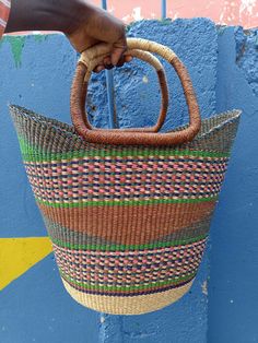 a hand holding a woven basket hanging from the side of a blue wall with yellow and green stripes