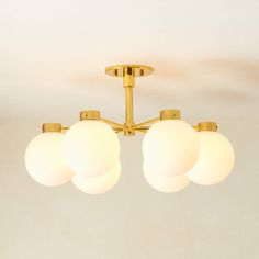 three white balls are hanging from a brass ceiling light in a room with beige walls