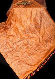 With design influences from the Mughals, the Royals of Kashmir and exquisite weaving techniques from China that were brought to India by Parsi merchants, comes the majestic Tanchoi Jamawar fabric! This pure Satin Silk Banarasi saree in a soft Marmalade shade of Orange  and features Tanchoi Jamawar paisley design in Green, Orange, and Red shades. Expertly woven with smooth and lustrous fabric, the saree showcases fine paisley patterns in complementary hues, with no cut or floating threads on the reverse side. SILK MARK CERTIFIED This saree is ready to wear with fall and pico done. Handmade silk tassels adorn the pallu and add more grace to it. An unstitched blouse fabric is included. *Note: There may be minor variations in the shade, the texture of the product. Hues/textures show differentl Silk Banarasi Saree, Red Shades, The Royals, Banarasi Saree, Paisley Design, Satin Silk, Banarasi Sarees, Shades Of Orange, Blouse Fabric