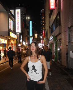 a woman standing in the middle of a street at night with her hands on her hips