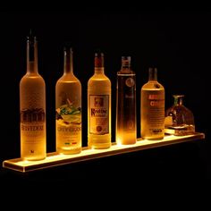 an assortment of liquor bottles are lit up on a wooden shelf in front of a black background