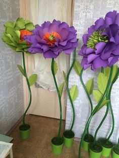 three purple flowers are in green vases on the floor next to a wall with white lace