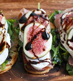 three sandwiches with figs, cheese and sauce on them sitting on a cutting board