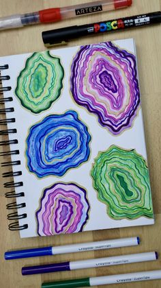 a spiral notebook with four different colored paper designs on it next to markers and pencils